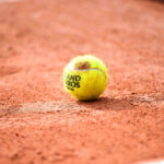 Balle de tennis de Roland Garros déposée au sol sur de la terre battue.