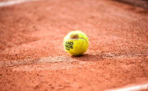 Balle de tennis de Roland Garros déposée au sol sur de la terre battue.