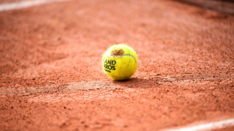 Balle de tennis de Roland Garros déposée au sol sur de la terre battue.