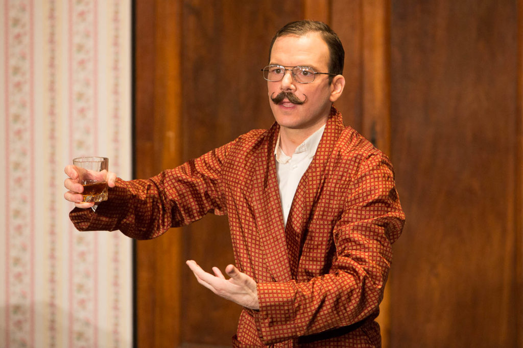 Sarkis Ohanessian est sur la scène du Théâtre Le Caveau dans "Thé à la menthe ou t'es citron". Il est vêtu d'un peignoir brun à carreaux et tient un verre d'alcool dans la main droite. Il porte des lunettes et une moustache.