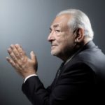 Dominique Strauss-Kahn est de profil, les mains jointes. Il porte un costume noir.