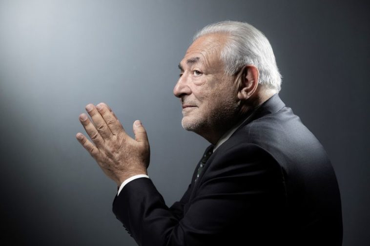 Dominique Strauss-Kahn est de profil, les mains jointes. Il porte un costume noir.