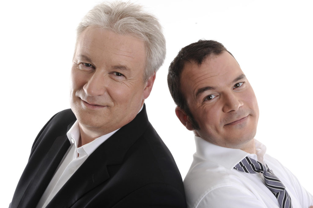 Sarkis Ohanessian et Philippe Robin, animateurs du Grand Quiz et son bêtisier 2009 à la Radio Télévision Suisse. Sarkis porte une chemise blanche et une cravate lignée de noir et gris. Les deux animateurs sont dos à dos et regardent l'objectif.