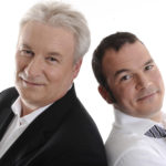Sarkis Ohanessian et Philippe Robin, animateurs du Grand Quiz et son bêtisier 2009 à la Radio Télévision Suisse. Sarkis porte une chemise blanche et une cravate lignée de noir et gris. Les deux animateurs sont dos à dos et regardent l'objectif.