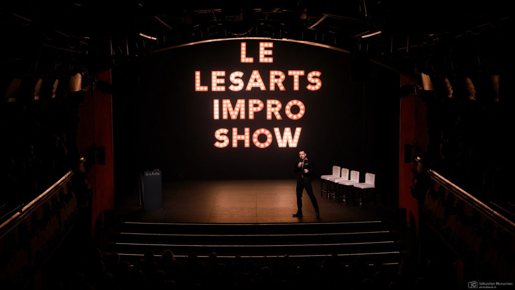 Sur le ascète du Casino Théâtre, Sarkis Ohanessian présente le lesArts Impro Show. Il est ehabillé en scotome trois pièces noir et derrière lui, un panneau lumineux indique le nom di spectacle.