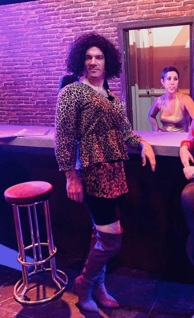 Sarkis Ohanessian est habillé en drag queen pour le spectacle "Sister Act" au théâtre Barnabé de Servion. Il porte une perruque noire frisée, un haut léopard, une jupe léopard et des bottes hautes à talons violettes.
