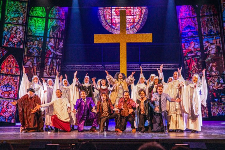 Saluts finaux du spectacle "Sister Act" au Théâtre Barnabé de Servion. Sarkis Ohanessian, qui interprète Monseigneur O'Hara, est en toge blanche . Il a les mains levées et chante, entouré de tous les comédiens de la troupe.