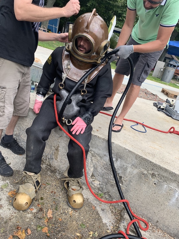 Sarkis Ohanessian porte un scaphandre. Des personnes s'affairent autour de lui pour fixer les différents tuyaux et câbles. Sarkis s'apprête à descendre dans le lac de Bienne.