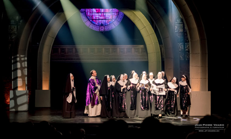 Sarkis Ohanessian est sur la scène du Théâtre Barnabé de Servion dans "Sister Act". Il est vêtu de blanc et de paillettes violettes. Il est avec les nonnes dans la scène de la revue de presse.