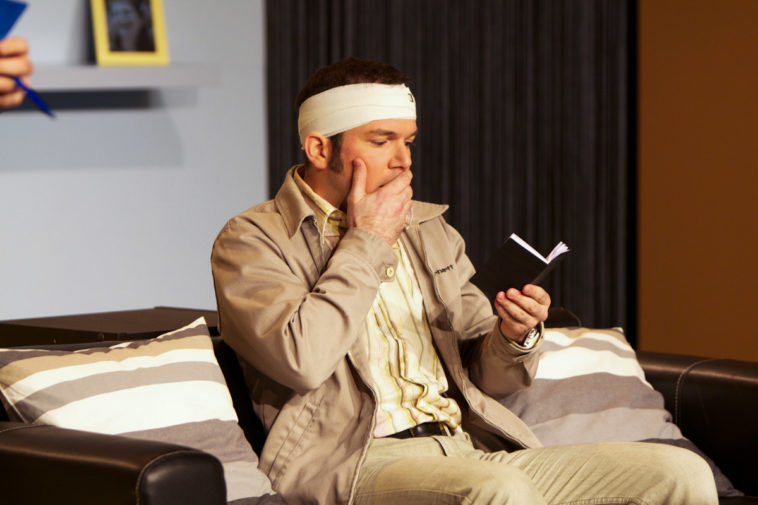 Sarkis Ohanessian, sur la scène du Théâtre le Caveau à Genève, joue "Stationnement Alterné", pièce de Ray Cooney. Il est habillé d'un pantalon gris, une chemise jaune et une veste grise. Il porte un bandage autour de la tête. Il regarde de manière effarée son agenda.