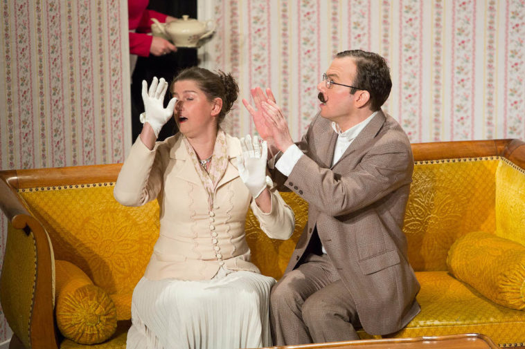 Sarkis Ohanessian est sur la scène du Théâtre Le Caveau. Il joue "Thé à la menthe ou t'es citron" de Patrick Haudecoeur. Il est assis sur un canapé jaune aux côté de Julie Despriet. Il porte des lunettes rondes et une moustache. Il est vêtu d'un costume gris.