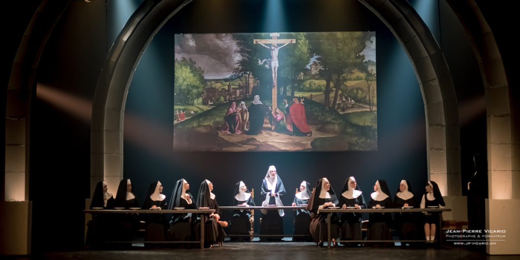 Les nonnes de Sister Act au théâtre Barnabé de Servion sont dans la scène du réfectoire. Derrière elle, une image biblique avec Jésus sur la croix est projetée.