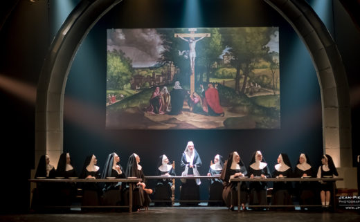 Les nonnes de Sister Act au théâtre Barnabé de Servion sont dans la scène du réfectoire. Derrière elle, une image biblique avec Jésus sur la croix est projetée.