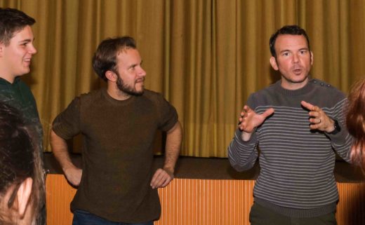 Photo couleur de Sarkis Ohanessian en train de donner une formation. Il est entouré de participants et leur explique quelque chose. Il est vêtu d'un pull brun rayé.