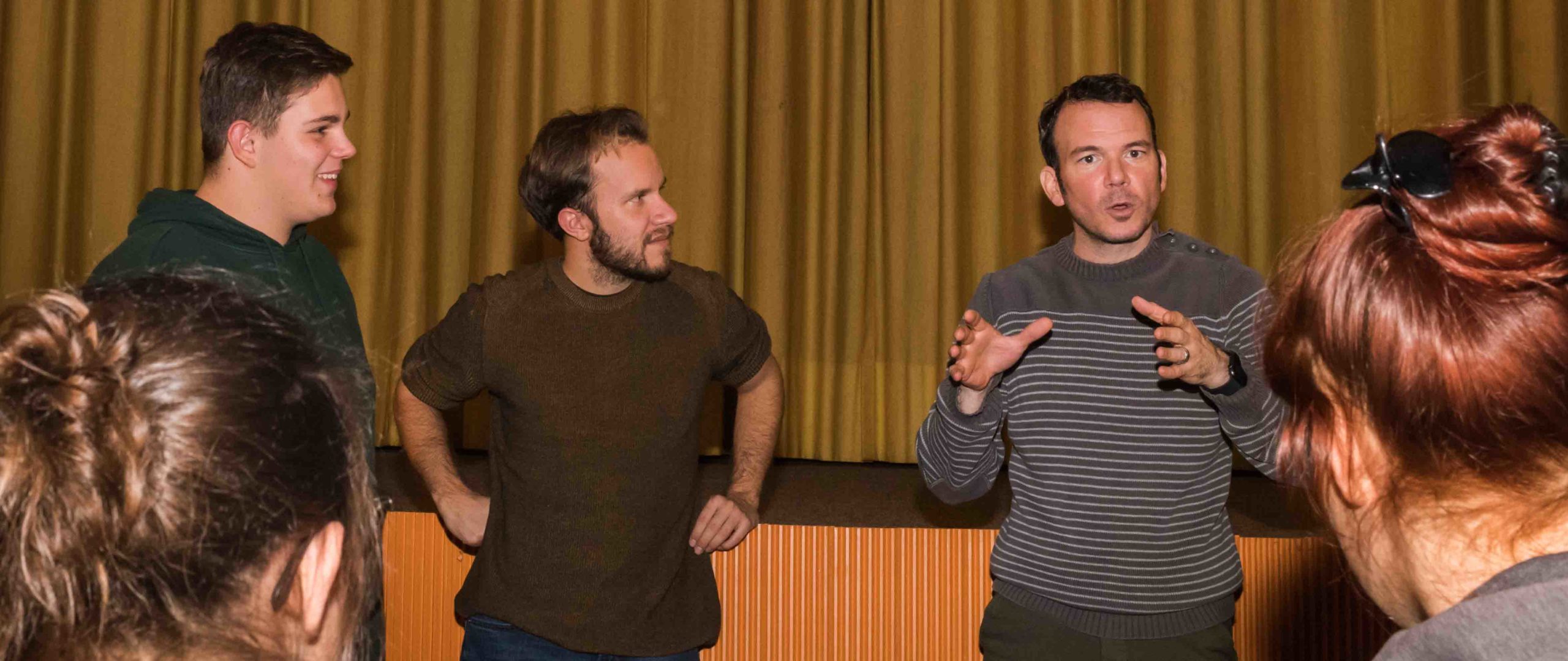 Photo couleur de Sarkis Ohanessian en train de donner une formation. Il est entouré de participants et leur explique quelque chose. Il est vêtu d'un pull brun rayé.