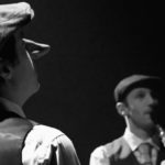 Image en noir et blanc montrant deux comédiens, un de dos avec un bey imposant (Cyrano) et un autre de face jouant de la clarinette